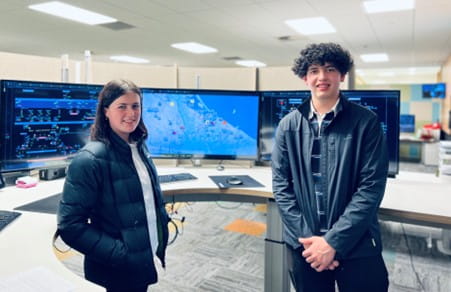 Two high school students, one male and one female, in front of computer screens