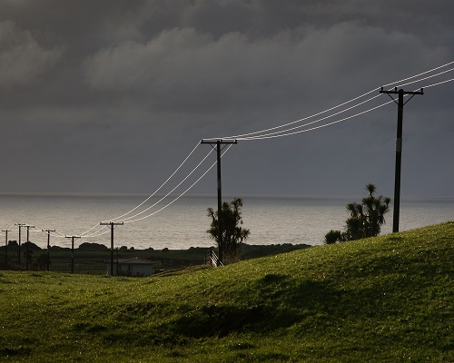 Landscape with dark skies, rural hills running to the sea, with power lines disecting the picture.