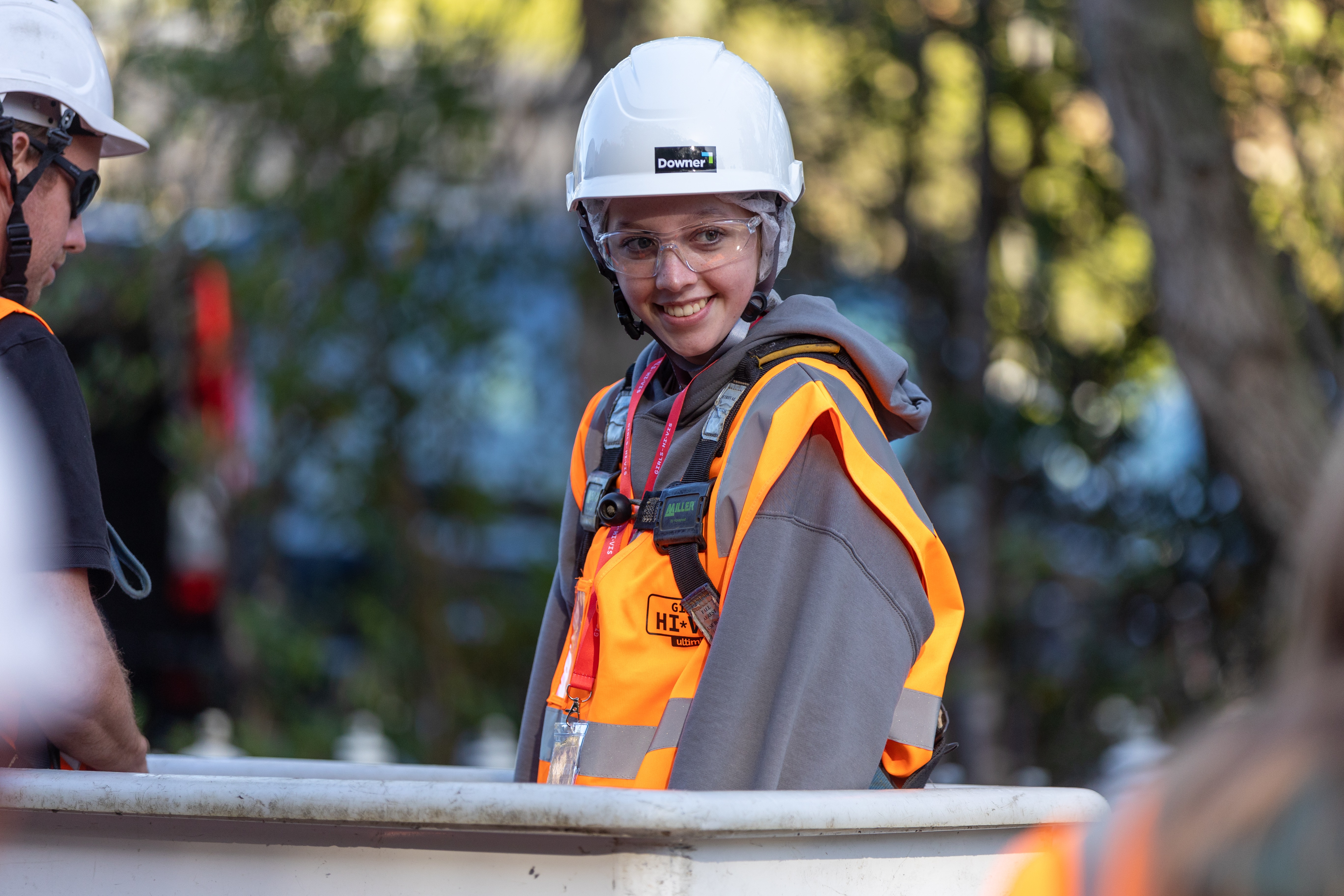 Female teenager with hard hat, safety glasses and hi-vis on standing in the bucket of a cherry picker