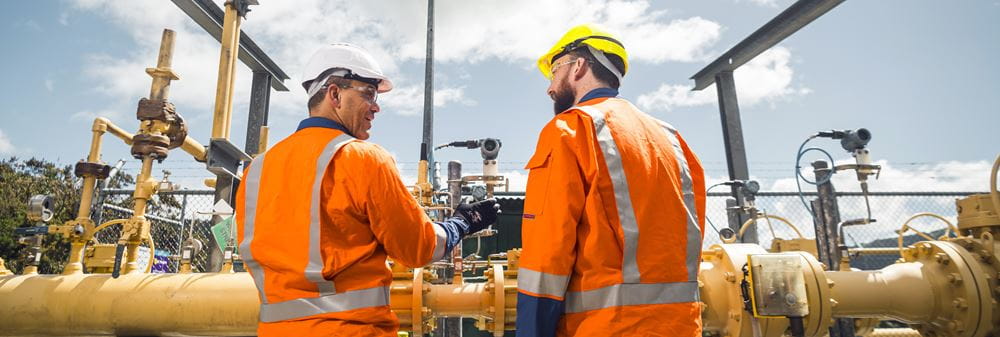 Two people in PPE in front of Powerco gas pipe infrastructure