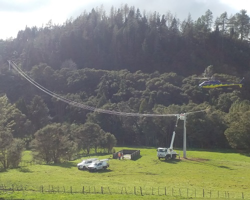 A helicopter being used to string lines between two power poles in a rural setting