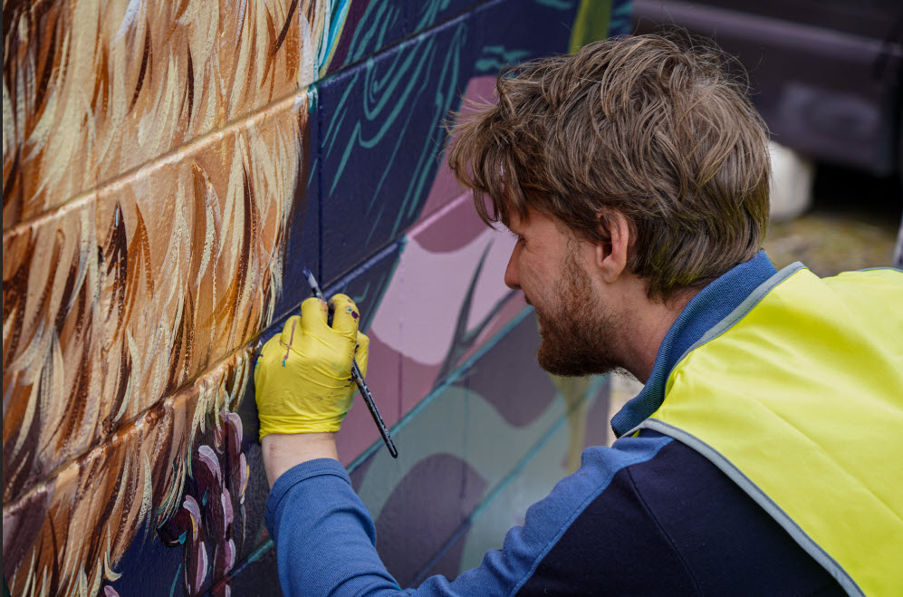 artist touching up paint on the Kauri Point substation mural