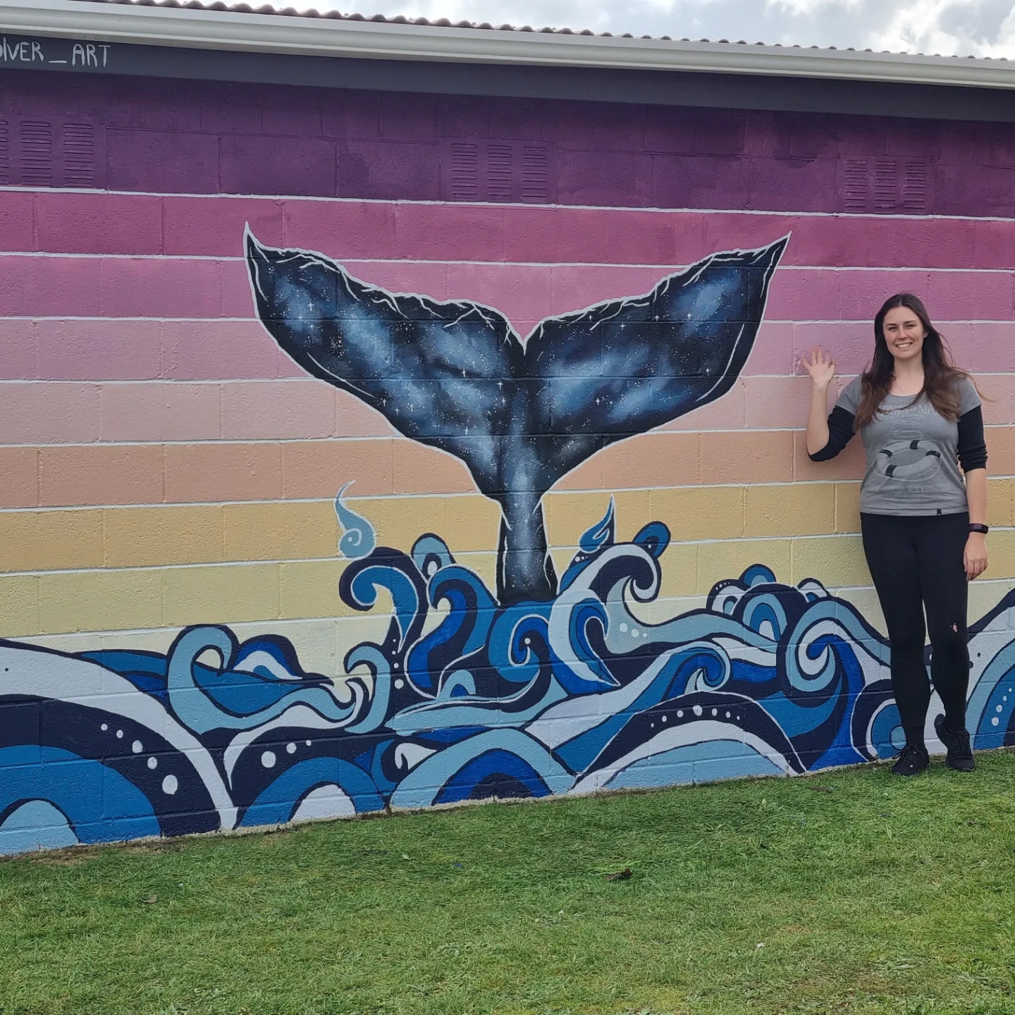 A woman in front of a mural featuring the tail of a whale in waves.