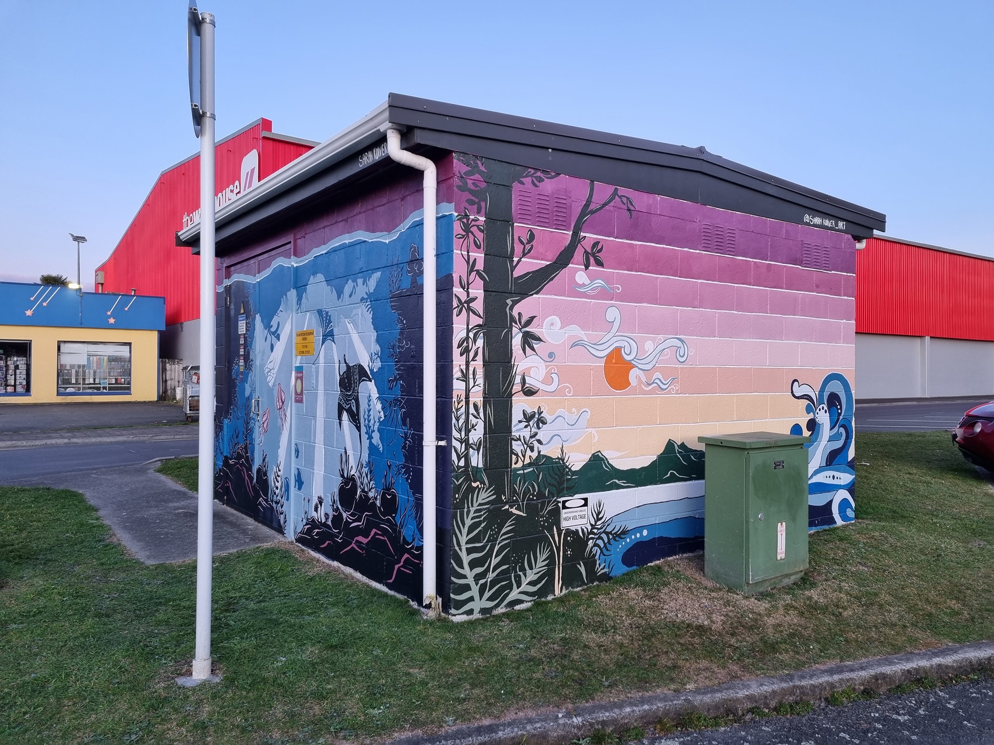 Two sides of a small concrete block building featuring a tropical scene mural.