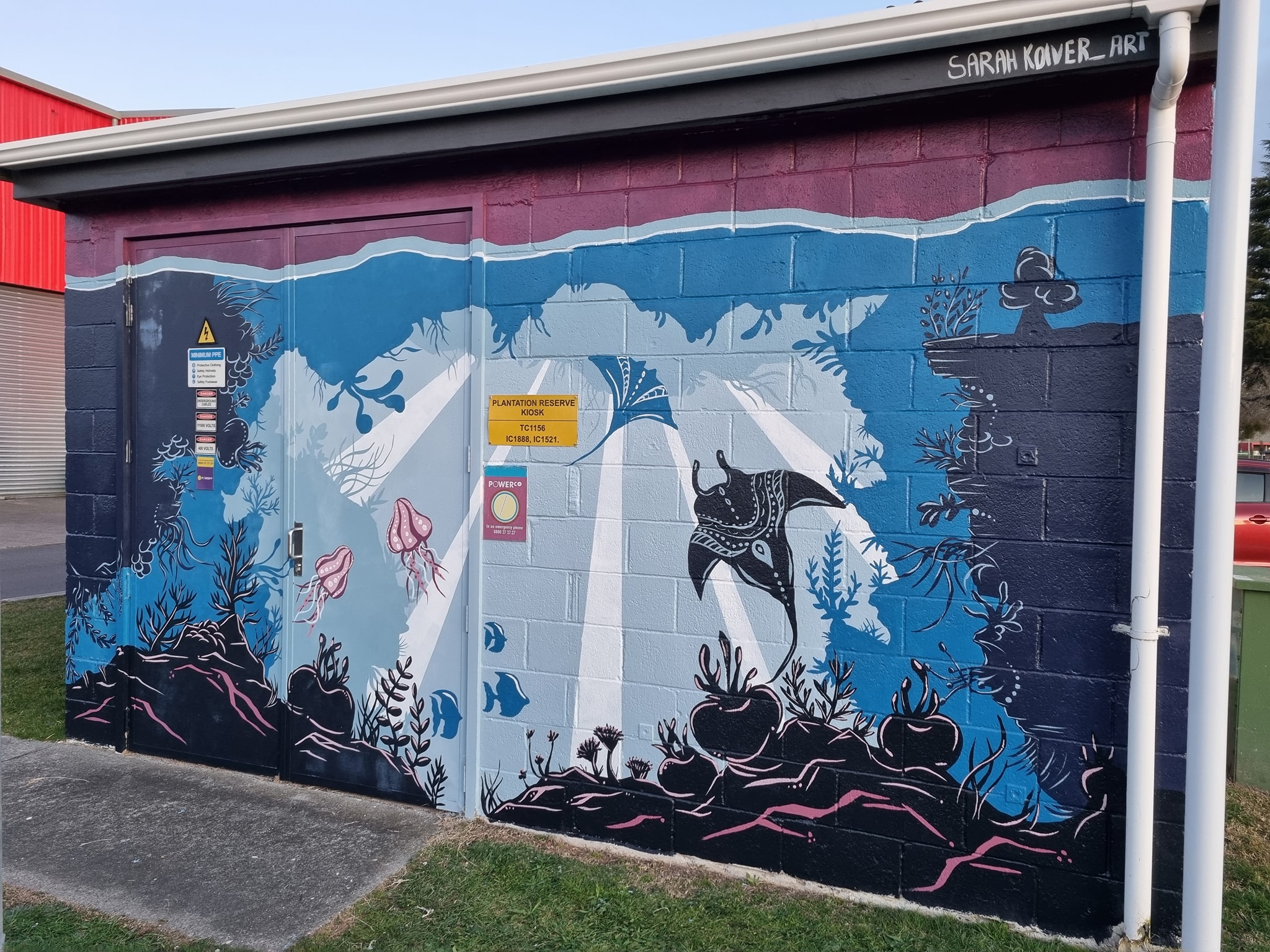 Mural on the side of a small concrete block building, showing underwater scene, including stingrays.