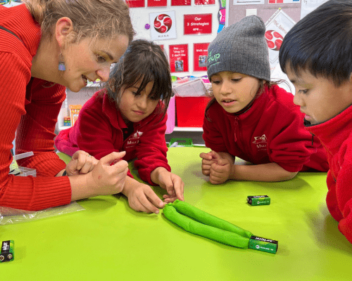 A teacher showing primary school students how to make an electricity circuit.