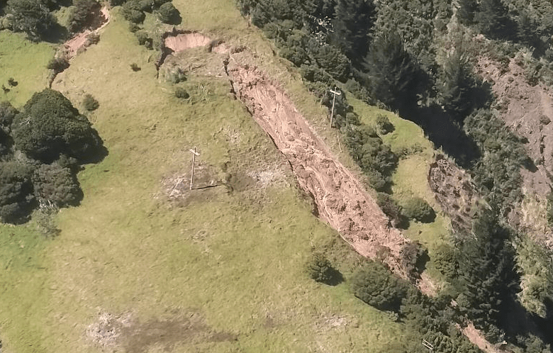 An aerial photo of rural land on a steep hillside with a large landslip going between two power poles