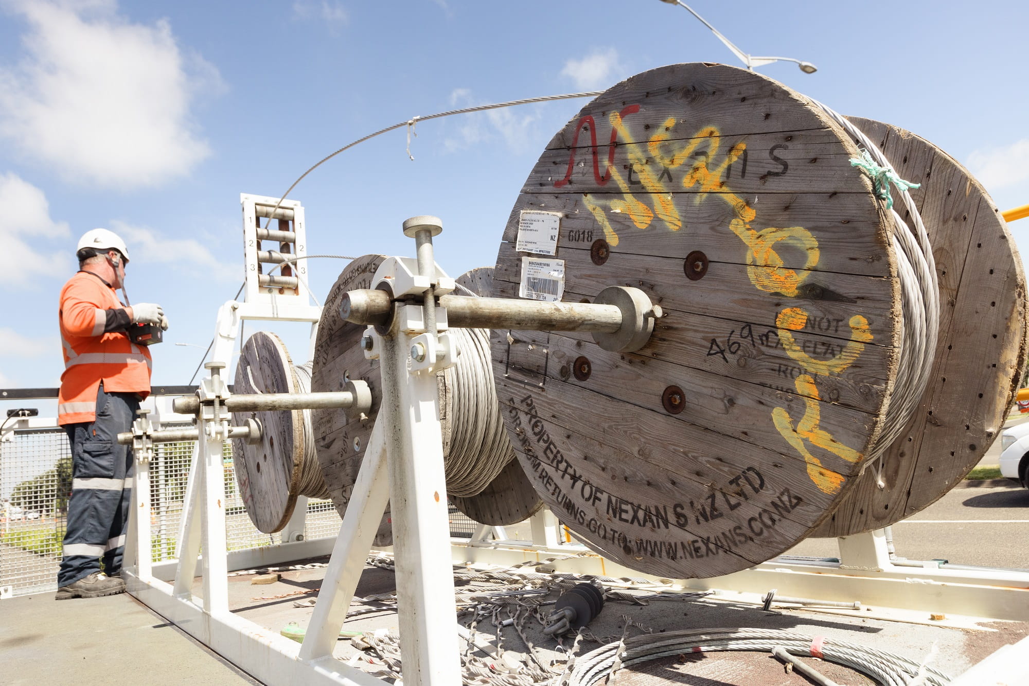 A faultman in PPE winding up a power line on a large cable spool.