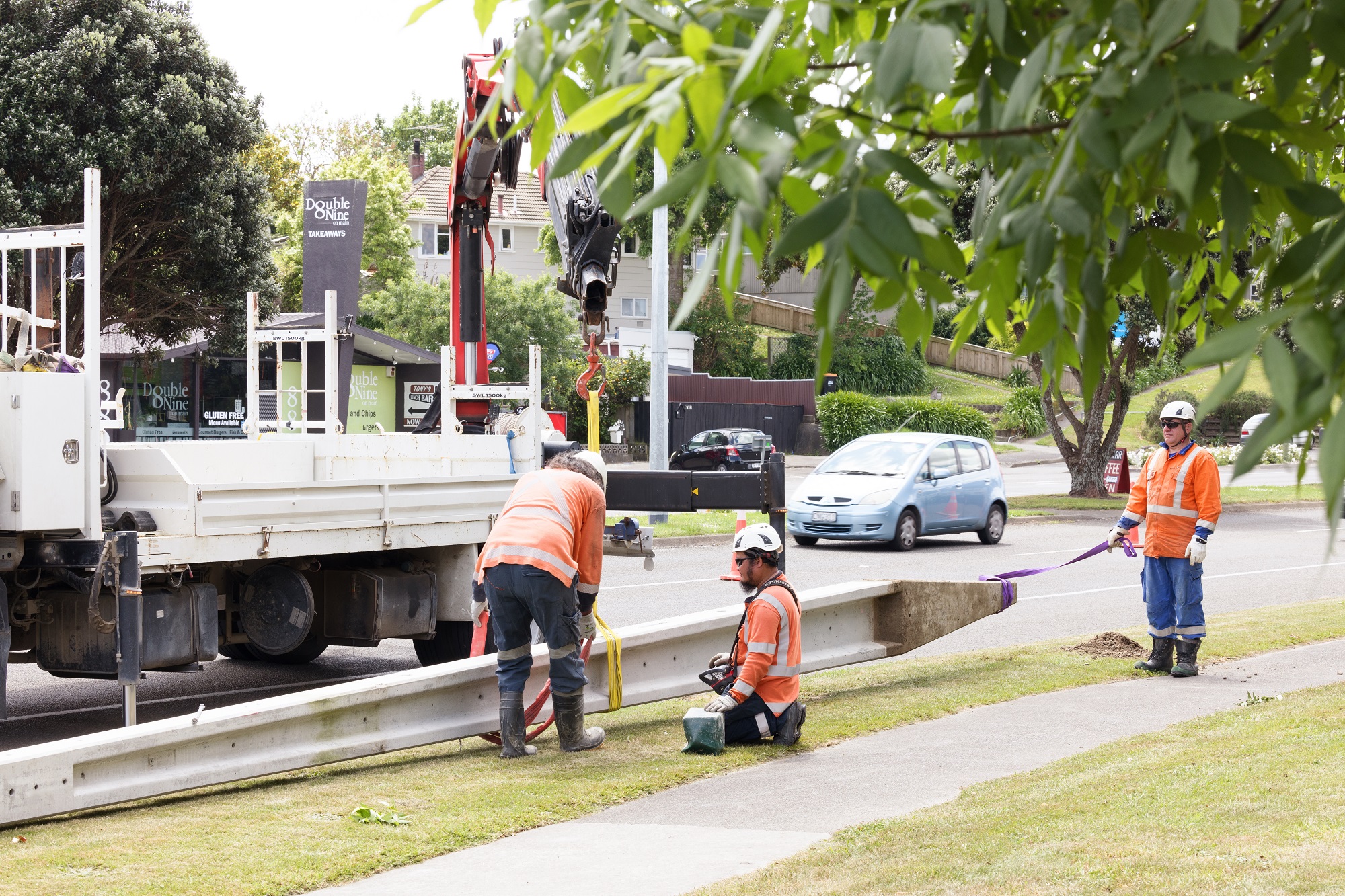 Workers in PPE on the side of the road with a power pole that is lying on the ground.