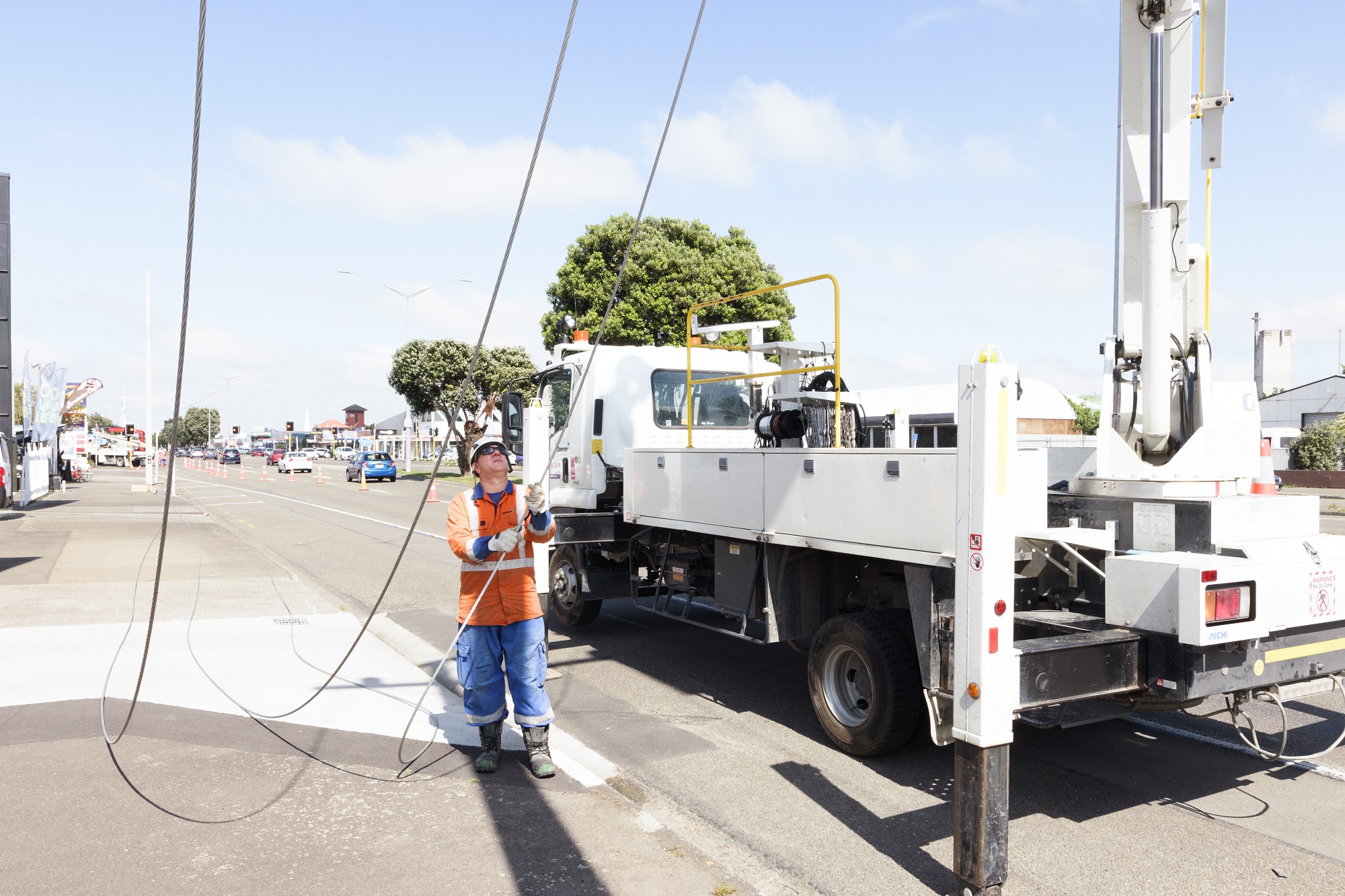 A worker in PPE pulling power lines down onto the path beside a work truck