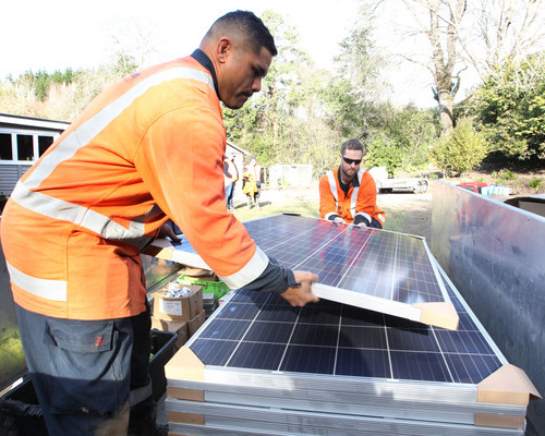 People in PPE lifting a solar panel from a stack of panels.